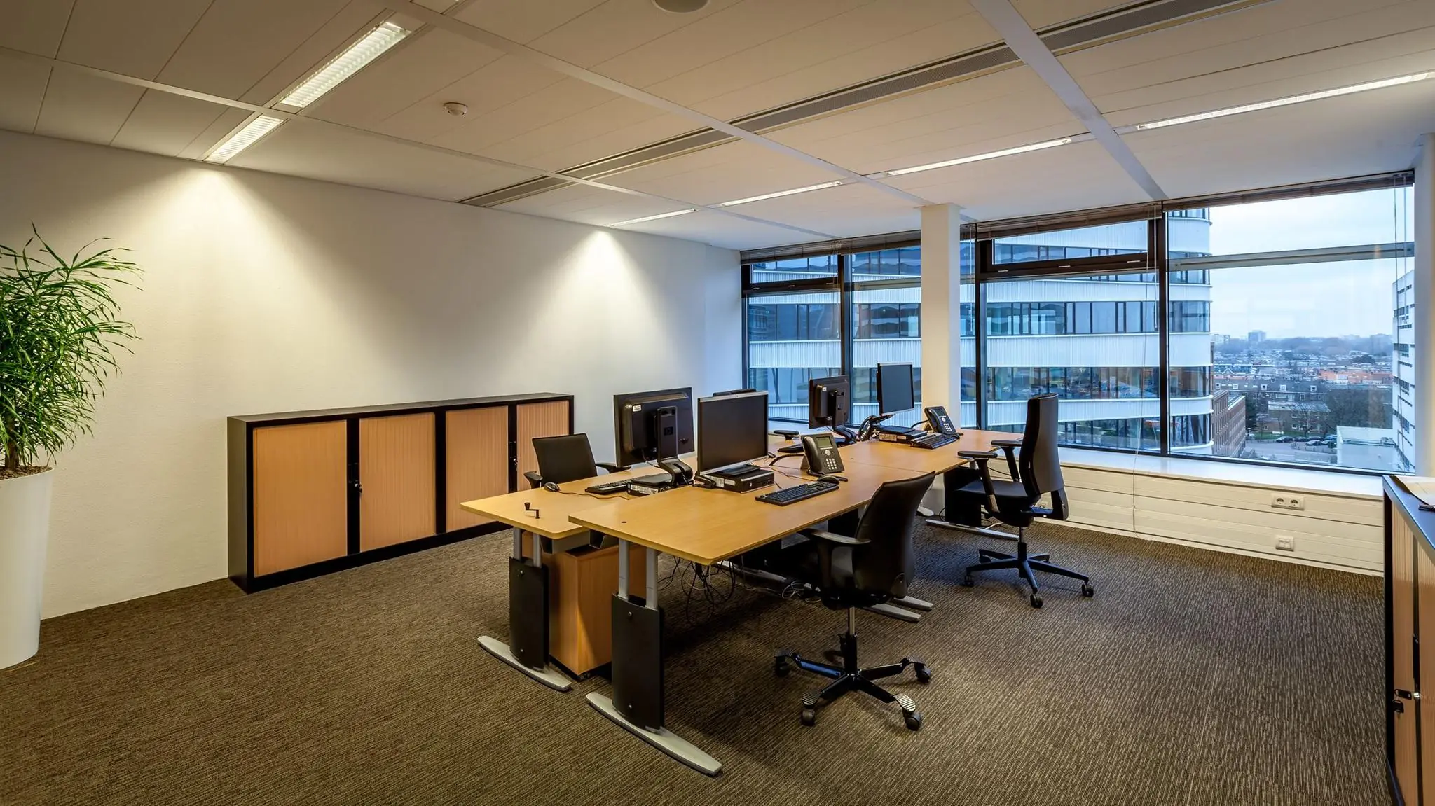 Modern kantoorbureau met meerdere werkplekken en uitzicht op de Prinses Beatrixlaan in Den Haag.